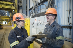 two aluminum workers in hard hats holding a shared clipboard in an aluminum plant