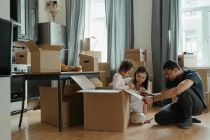 photograph of a man and woman helping a child with her homework, in. house surrounded by cardboard boxes