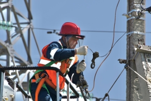 image of man in red hard hat pulling a wire at a transmission station
