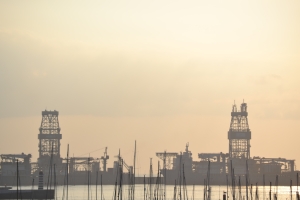 photograph of offshore oil drills under a yellow and faded sunsetting sky