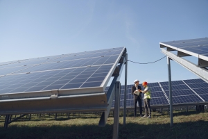 image of solar installers on a green field looking at a blueprint behind two giant angled solar panels