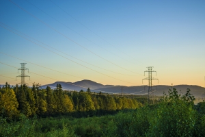 powerlines in front of mountains, green treescape, and mostly-blue sunsetting sky